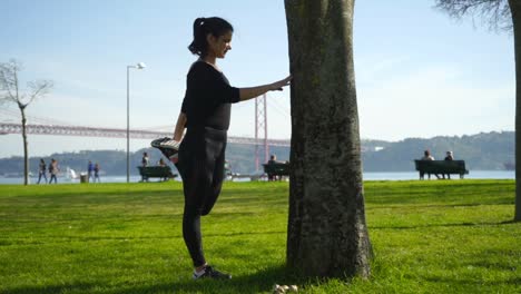 Sportswoman-leaning-at-tree-and-stretching-leg